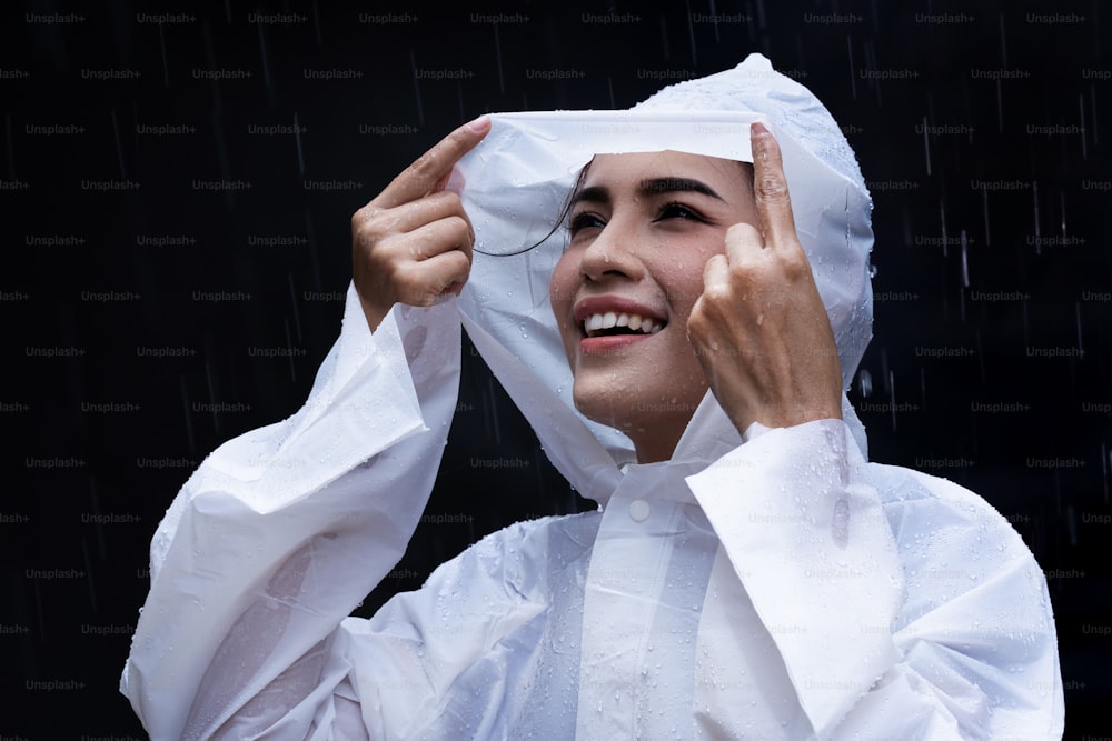 Mulher asiática do dia chuvoso vestindo uma capa de chuva ao ar livre. Ela está feliz.