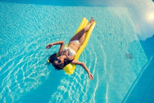 Belle femme, elle porte un bikini et dort sur un matelas pneumatique à la piscine d’été.