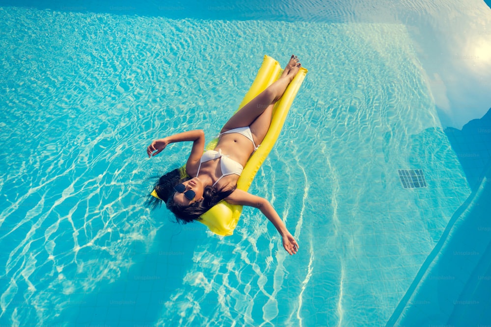 Hermosa mujer, lleva un bikini y duerme en un colchón de aire en la piscina de verano.