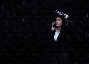 La mujer asiática está usando bolsas a prueba de lluvia, la lluvia está cayendo.ella está hablando por teléfono