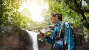 Asiatische Frauen Verwenden Sie das Telefon während eines Ausflugs in den Wald und Wasserfall.