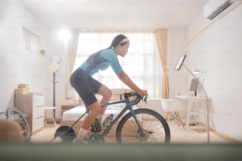 Mujer asiática Montar en bicicleta en línea entrenador en el dormitorio