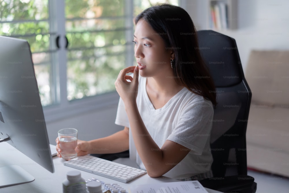 Asian woman Currently taking medicine While working at a computer desk, she is working home.
