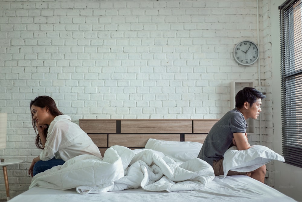 Casais asiáticos brigam sentados na cama, eles argumentam para não falar um com o outro. Eles estão infelizes