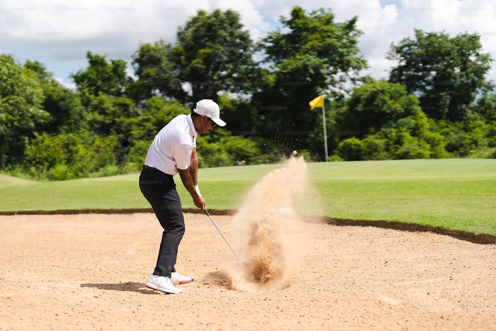코스에서 골프를 치는 아시아 남자. 그는 모래밭에서 골프공을 친다.