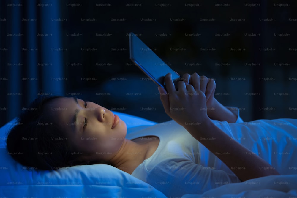 Asian women are using the tablet on the bed before she sleeping at night. Mobile addict concept.