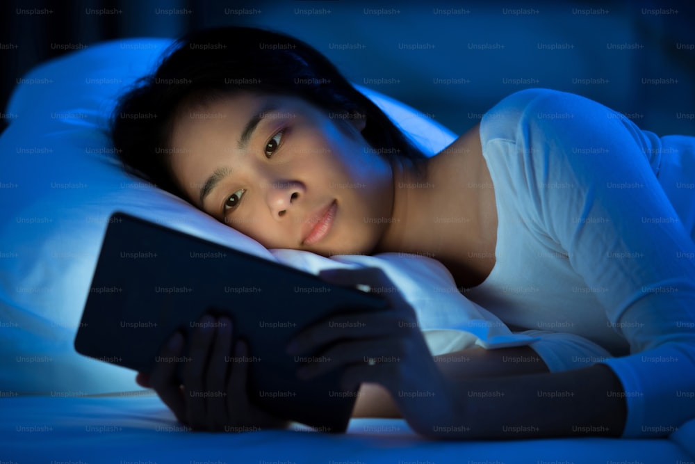 Les femmes asiatiques utilisent la tablette sur le lit avant de dormir la nuit. Concept de dépendance mobile.