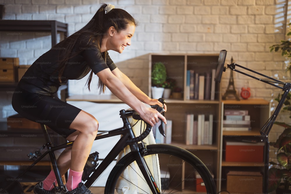 Asiatische Radfahrerin. Sie trainiert im Haus. Durch Radfahren auf dem Trainer und Online-Fahrradspiele