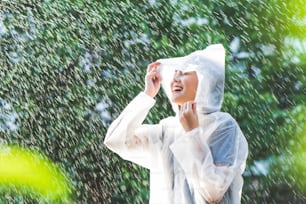Donna asiatica del giorno di pioggia che indossa un impermeabile all'aperto. Lei è felice.