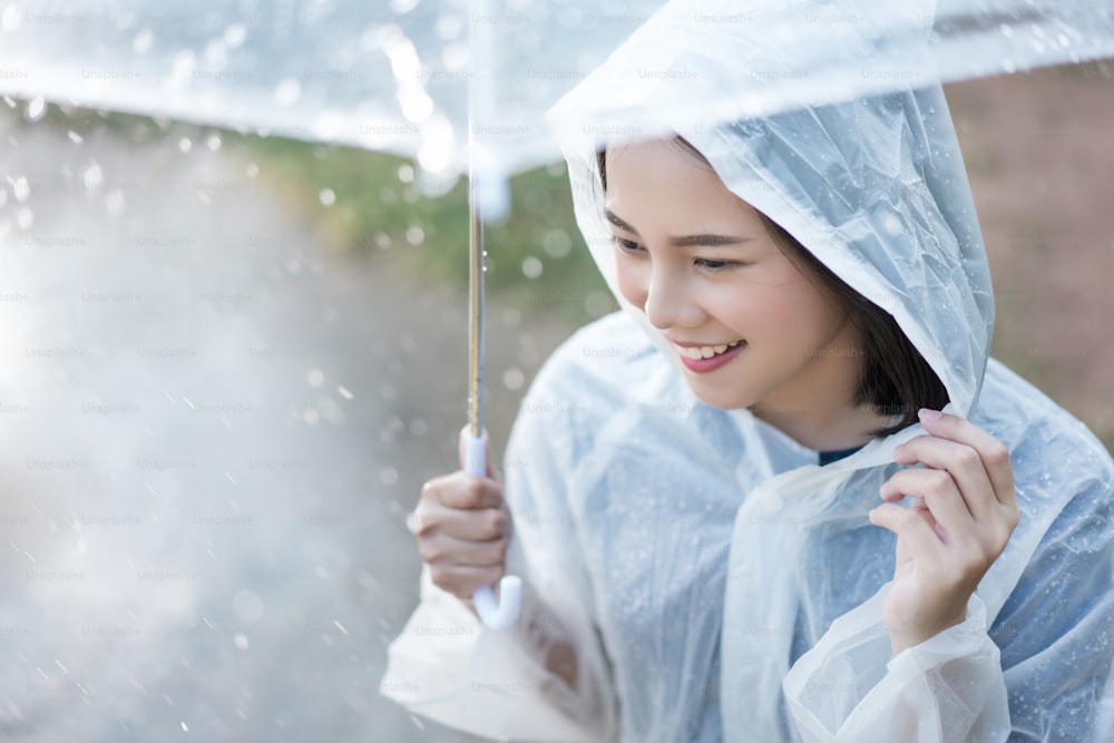 Rainy day asian woman wearing a raincoat outdoors. She is happy.