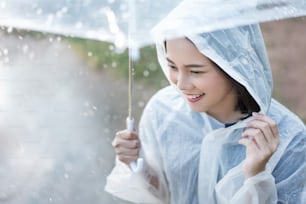 Mujer asiática de día lluvioso con un impermeable al aire libre. Ella está feliz.