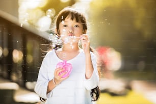 Menina asiática pequena está soprando uma bolha de sabão