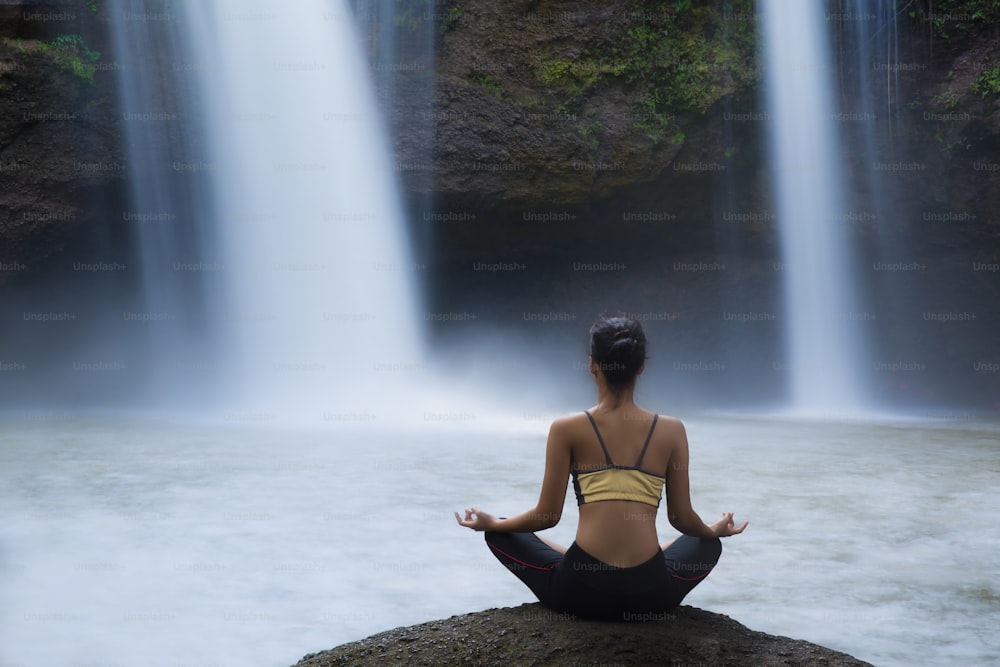 Mujer joven en una pose de yoga en la cascada, se sintió relajada. El ejercicio
