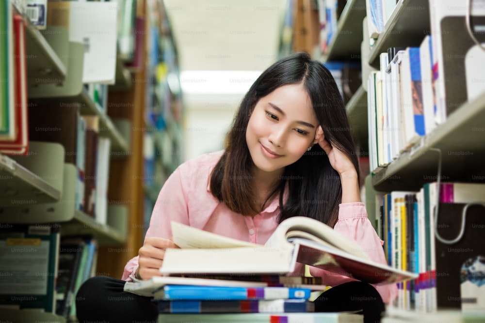 Asiatischer Student las in der Bibliothek. Sie ist glücklich und lächelt genossen