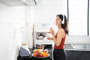 Donna asiatica che fa frullato di frutta dopo l'esercizio. Sta ascoltando musica