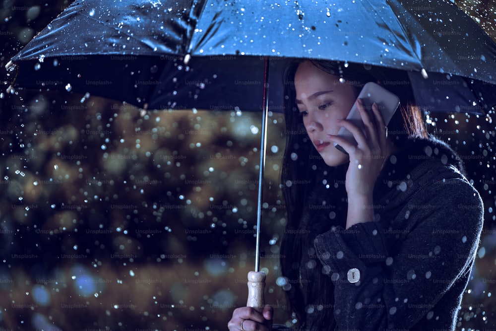 Las mujeres asiáticas están usando paraguas, la lluvia está cayendo. Ella está llamando