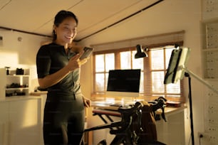 Ciclista asiática, está haciendo ejercicio en casa. Ella monta un simulador de bicicleta.