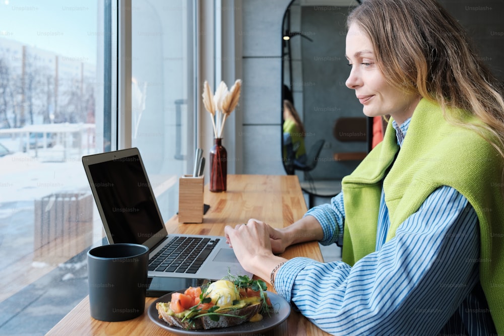 노트북과 음식 접시가 있는 테이블에 앉아 있는 여자