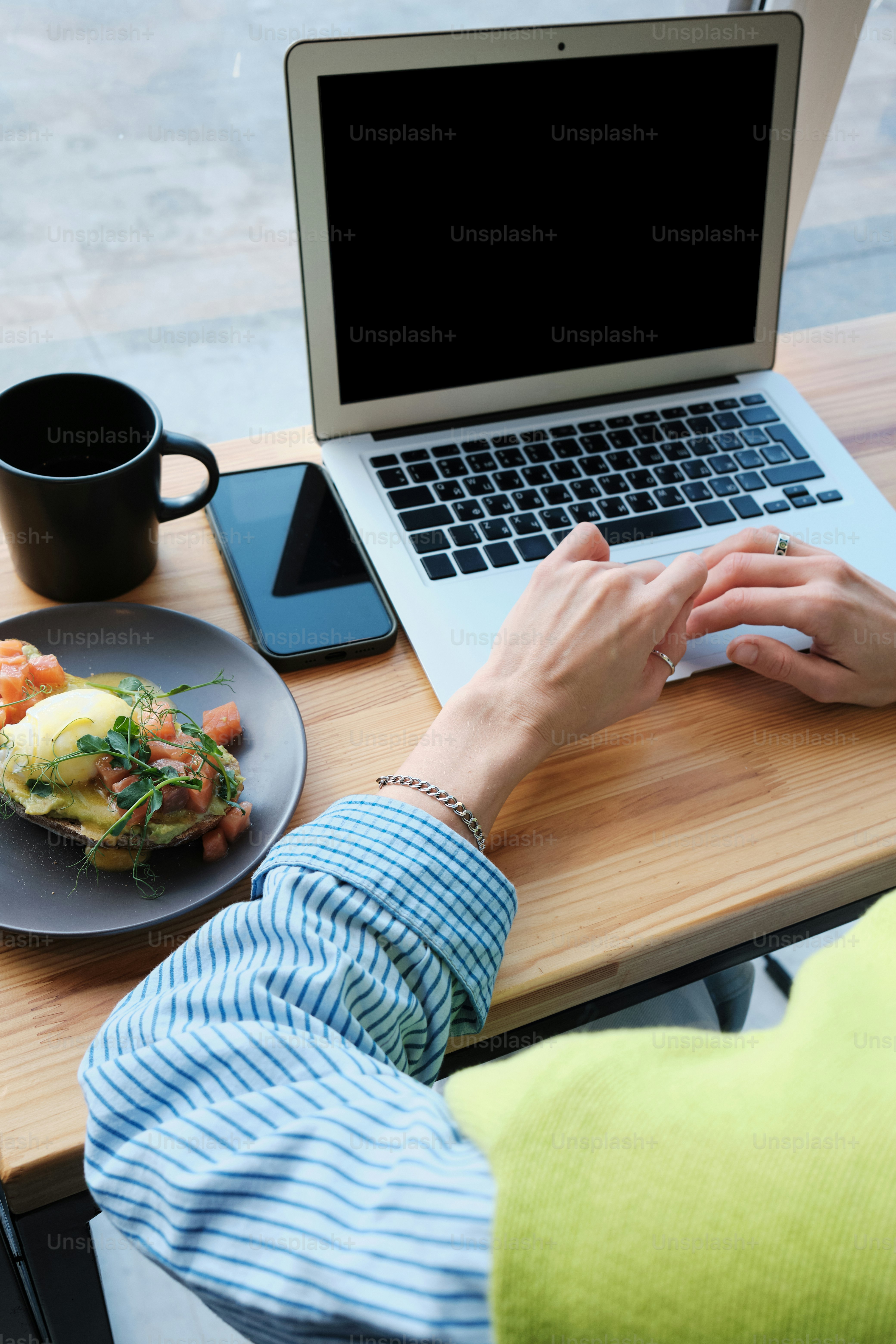 une personne assise à une table avec un ordinateur portable et une assiette de nourriture