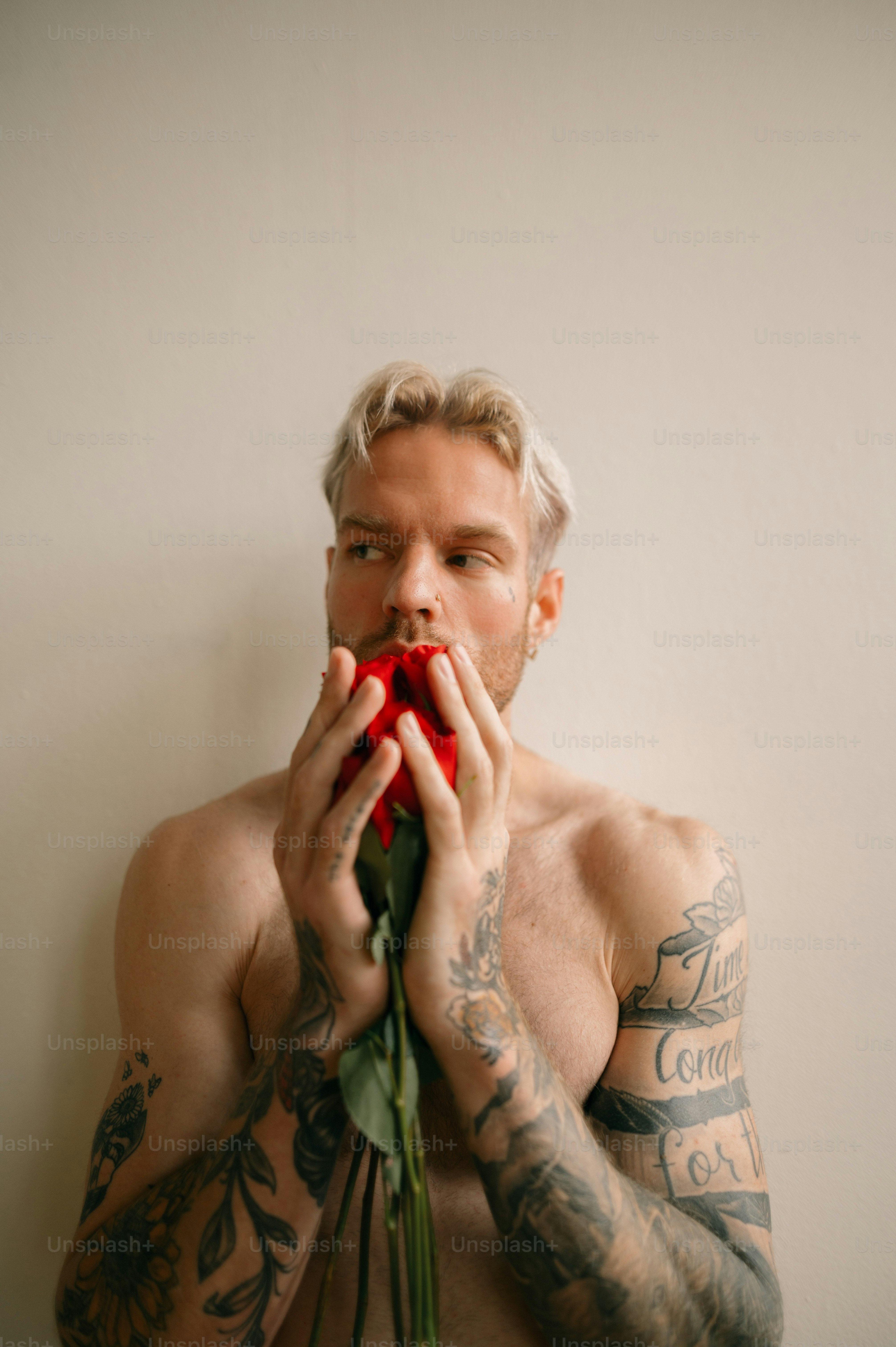 Eine Person mit Tätowierungen, die einen roten Gegenstand vor den Mund hält