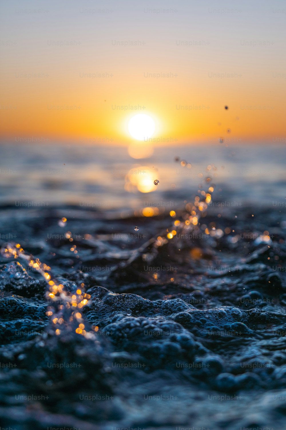 a close up of water with a sunset in the background