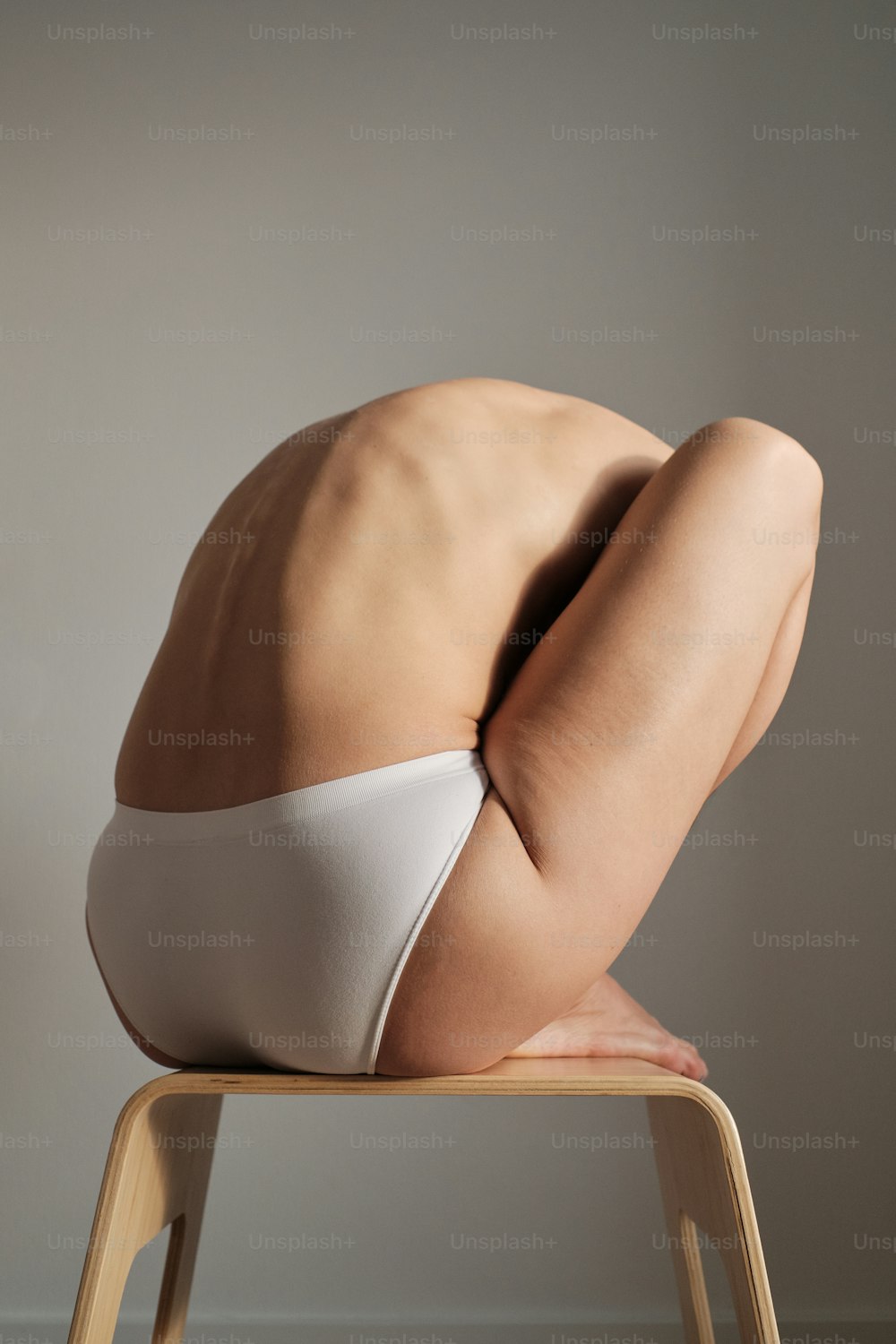 Eine nackte Frau im weißen Bikini sitzt auf einem Holzstuhl