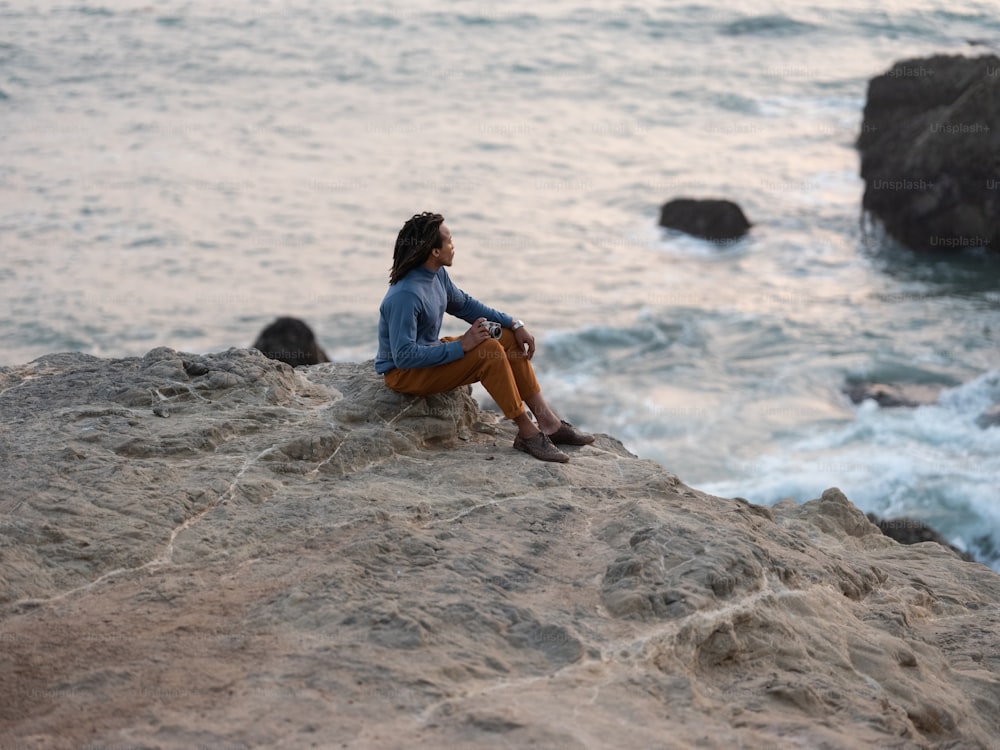 Ein Mann sitzt auf einem Felsen am Wasser