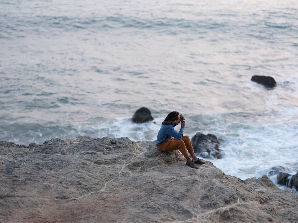 uma pessoa sentada em uma rocha à beira da água