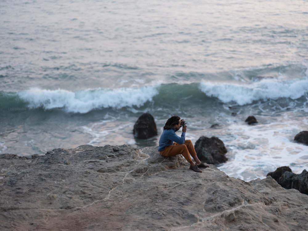 Eine Person, die auf einem Felsen am Meer sitzt