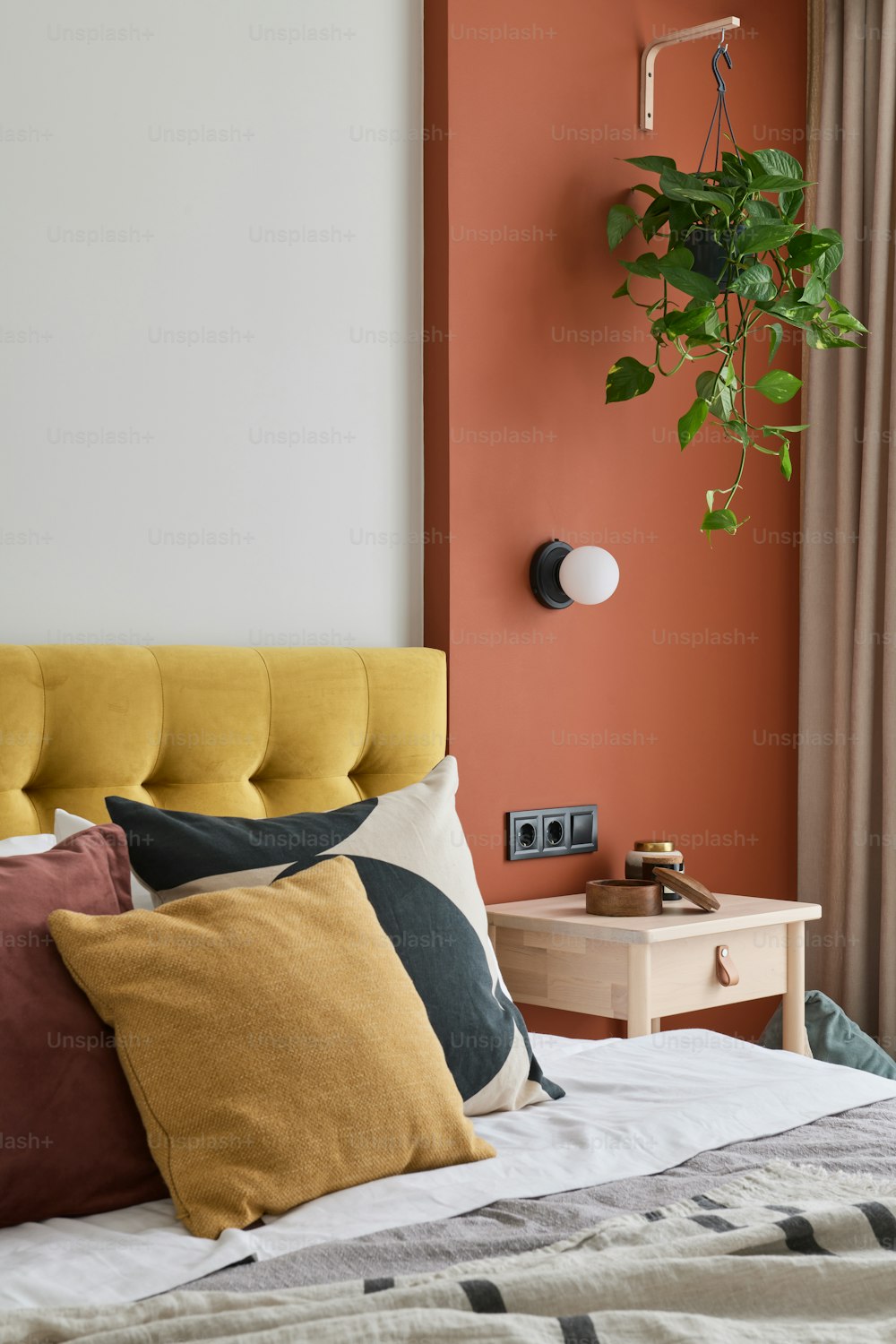 uma cama com um travesseiro amarelo e laranja e uma planta na parede