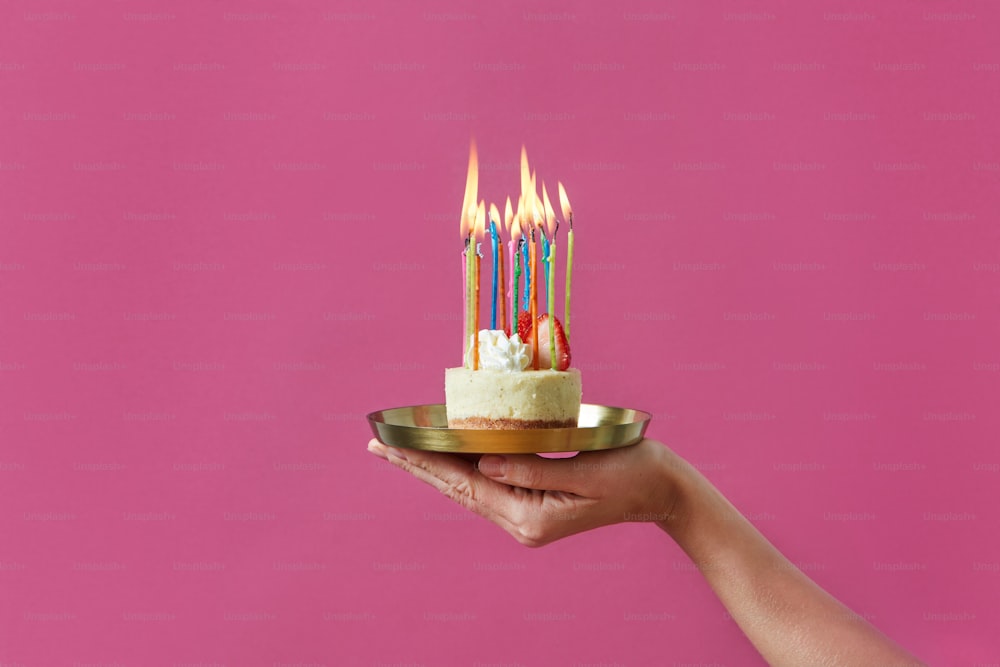 a hand holding a plate with a cake with candles on it
