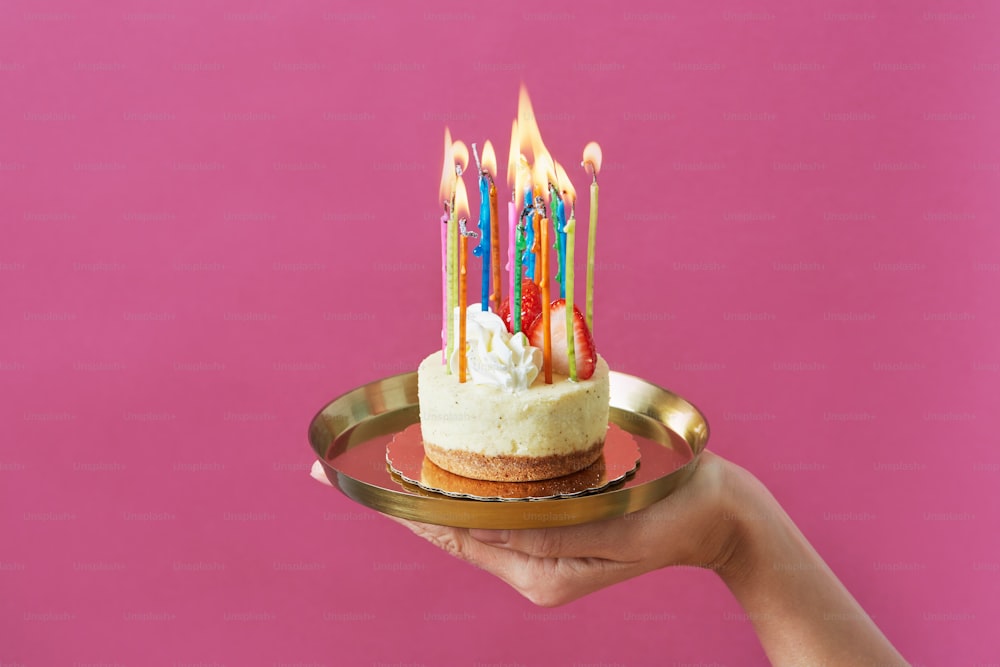 a hand holding a plate with a cake with candles on it