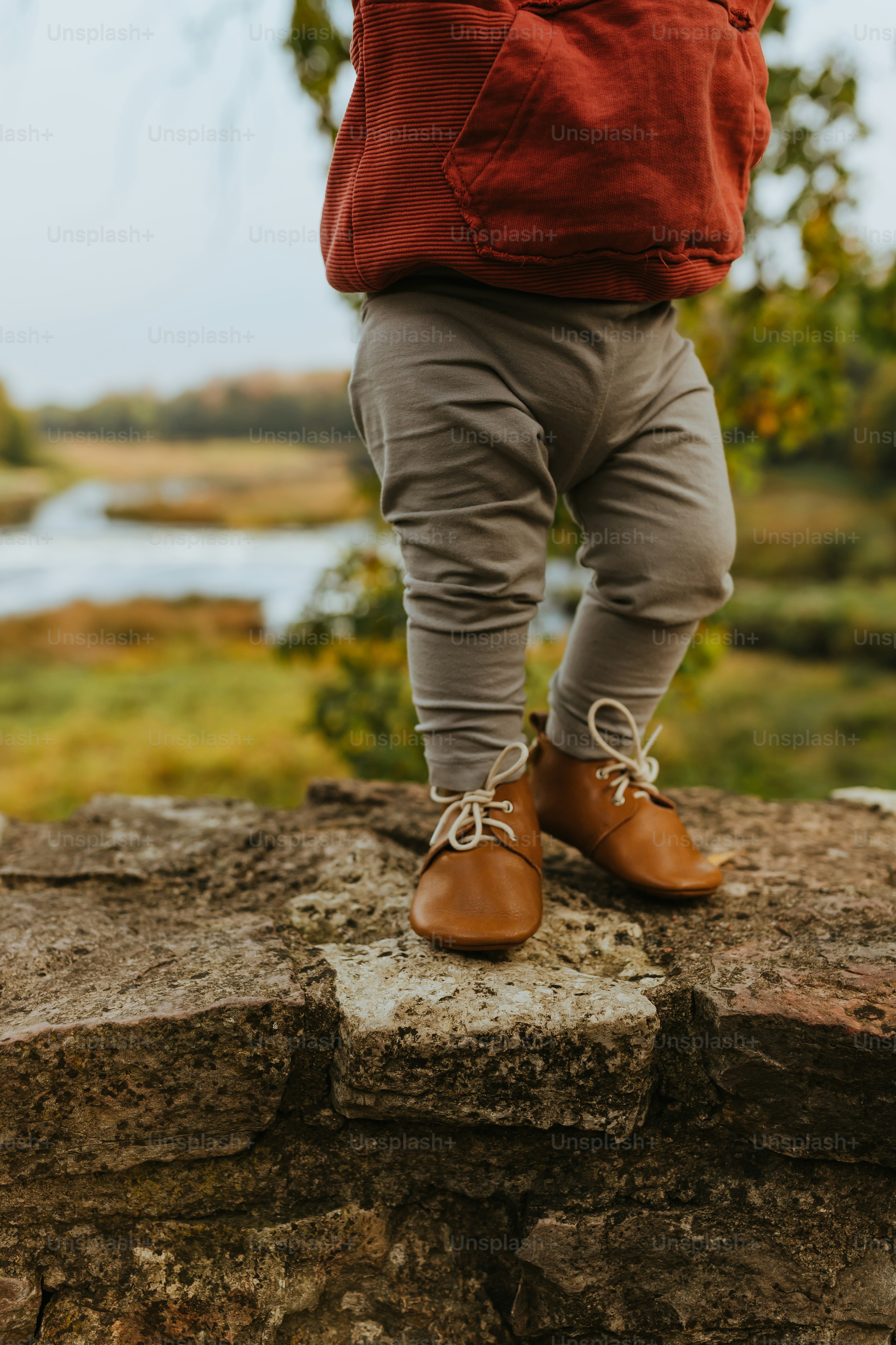 a person standing on a rock with a red jacket and brown shoes