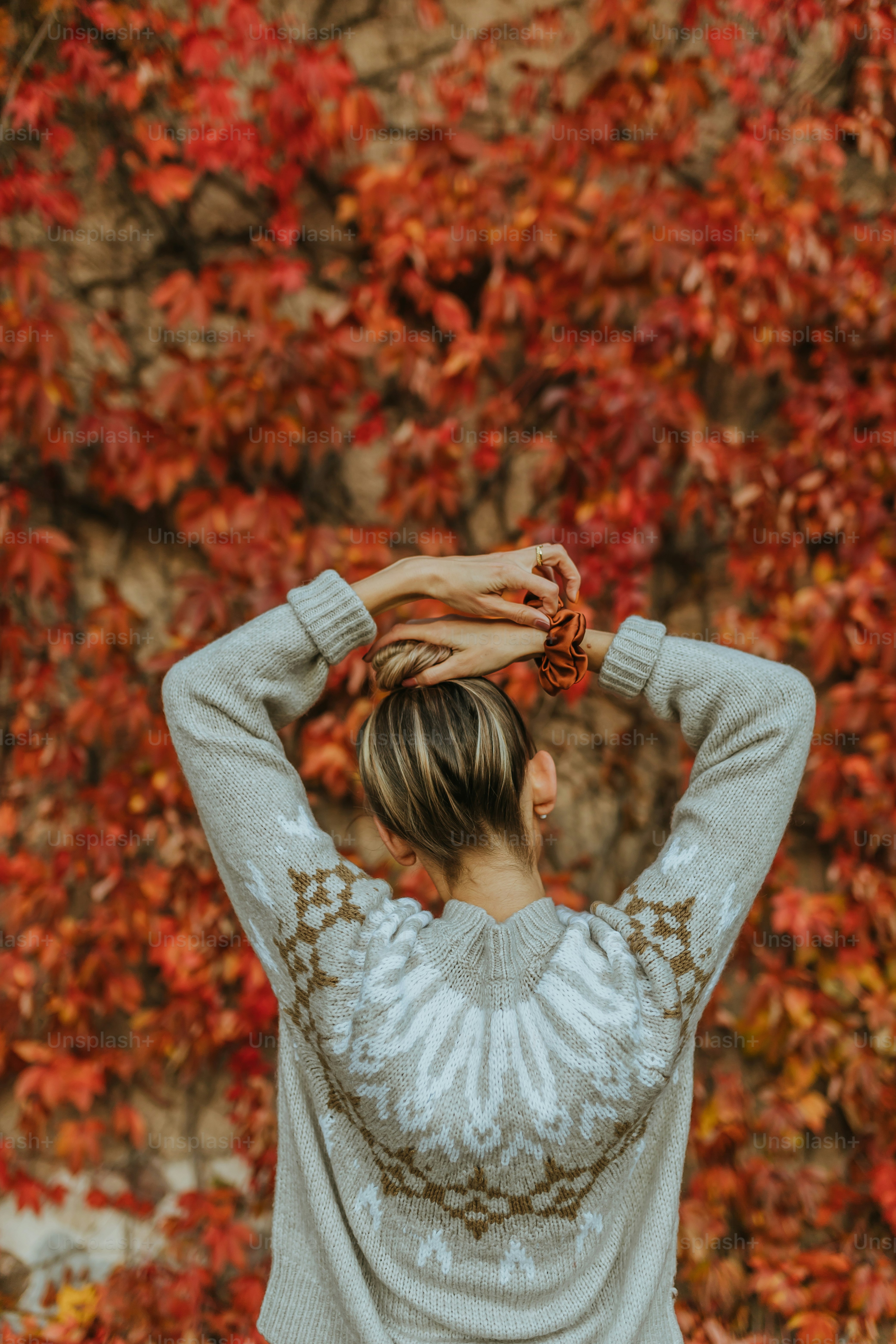 a man holding his hands up in front of a tree with red leaves