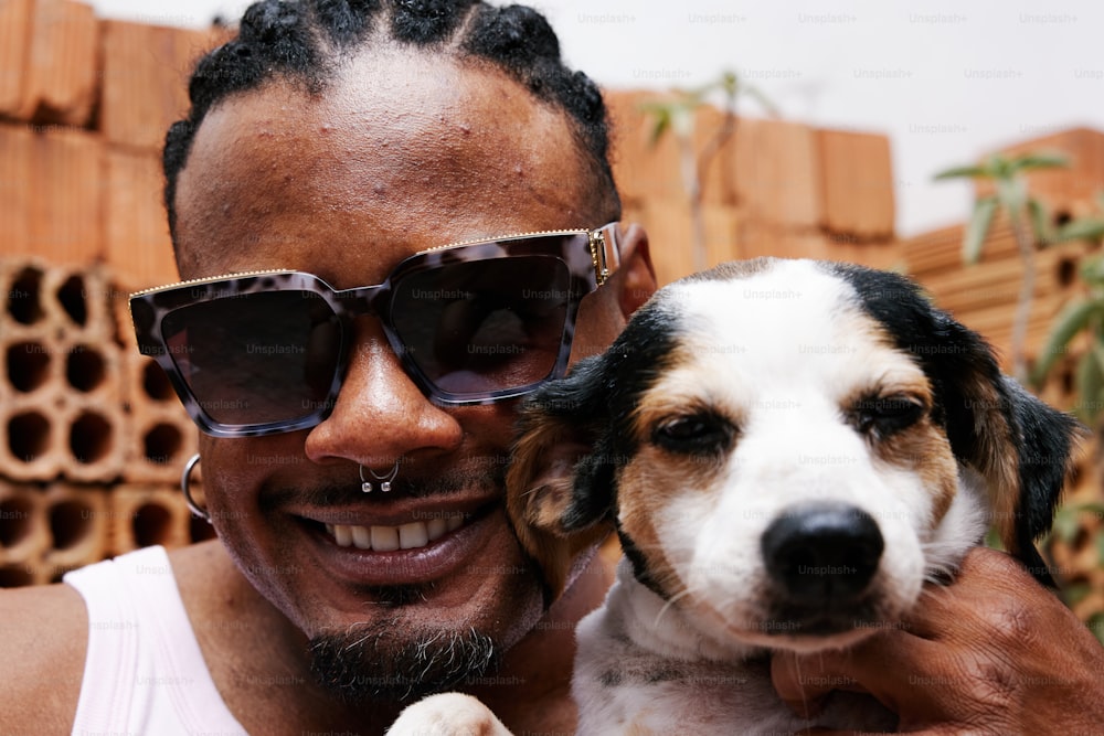 Un homme tenant un petit chien portant des lunettes de soleil