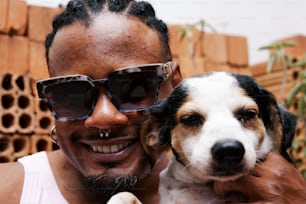 Un hombre sosteniendo a un perro pequeño con gafas de sol