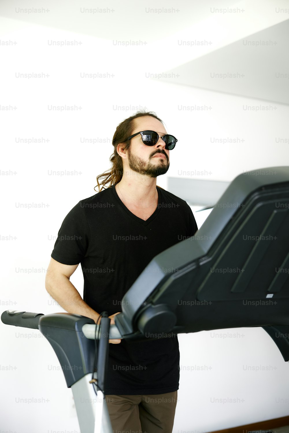 Un hombre con cabello largo y gafas de sol de pie junto a una cinta de correr