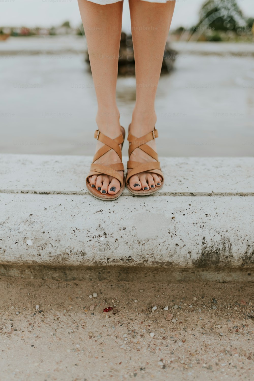 a woman's feet in sandals standing on a ledge