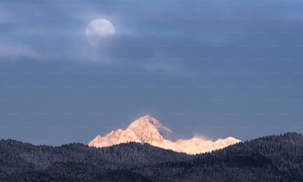 the moon is setting over a mountain range