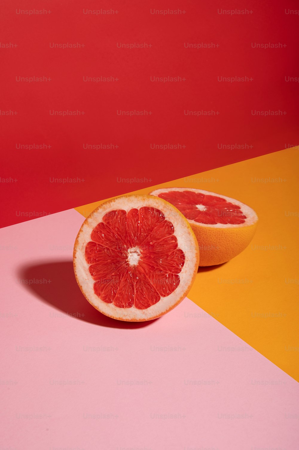 eine in zwei Hälften geschnittene Grapefruit auf rosa und gelbem Hintergrund