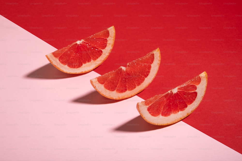 drei Scheiben Grapefruit auf rosa und rotem Hintergrund