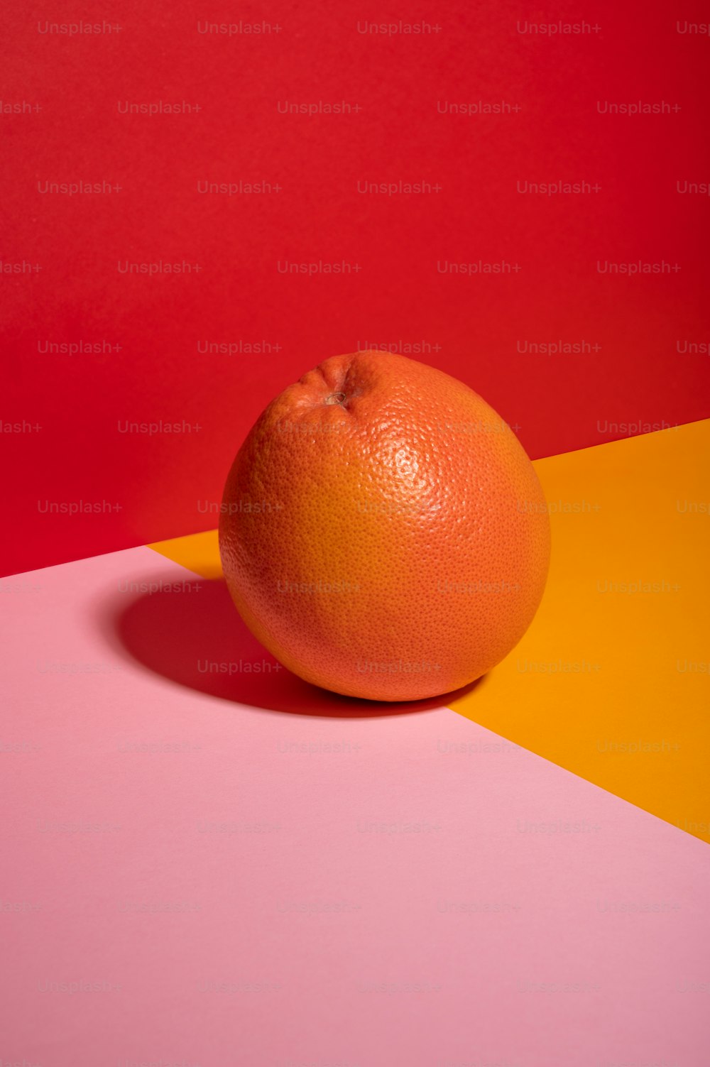 eine Orange, die auf einem rosa und gelben Tisch sitzt