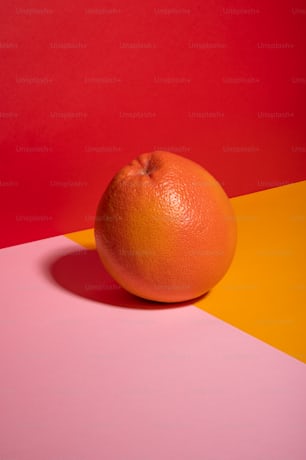 an orange sitting on top of a pink and yellow table