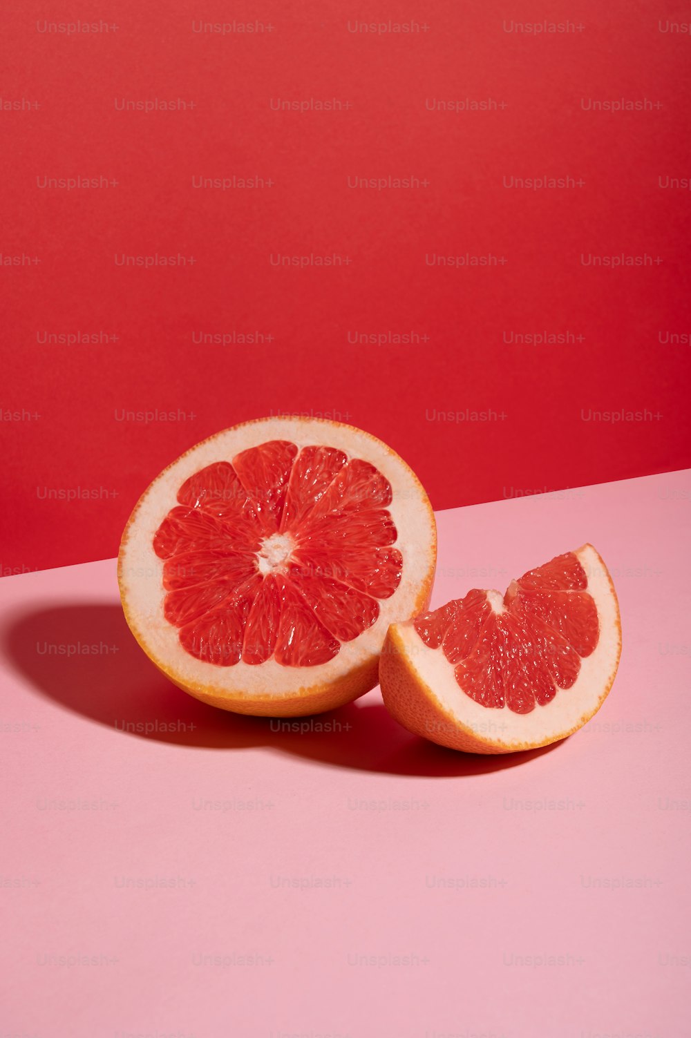 a grapefruit cut in half on a pink surface