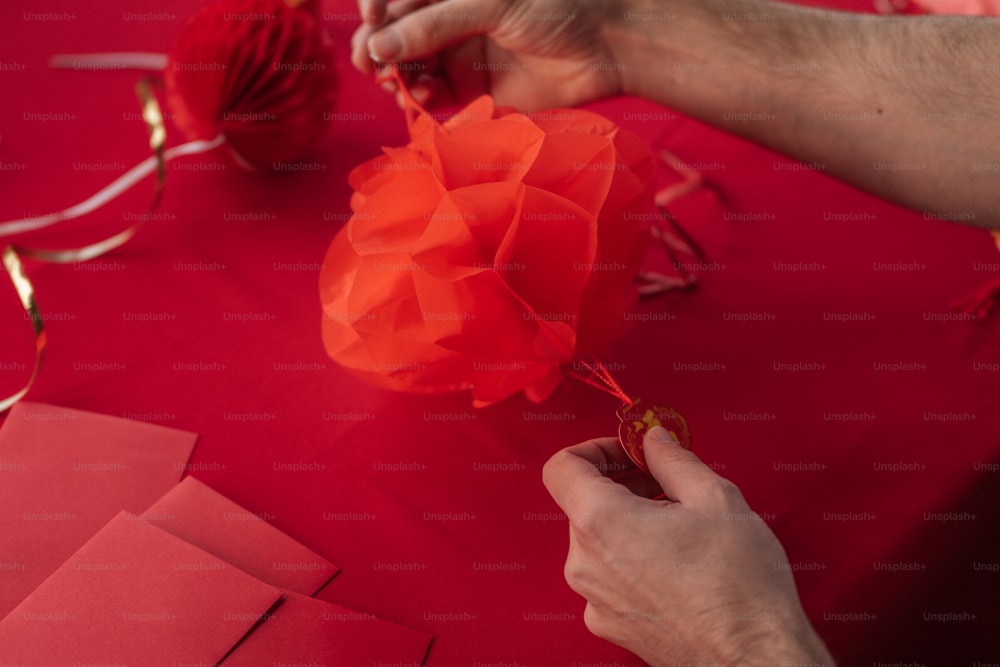 a person is making a paper flower out of red paper