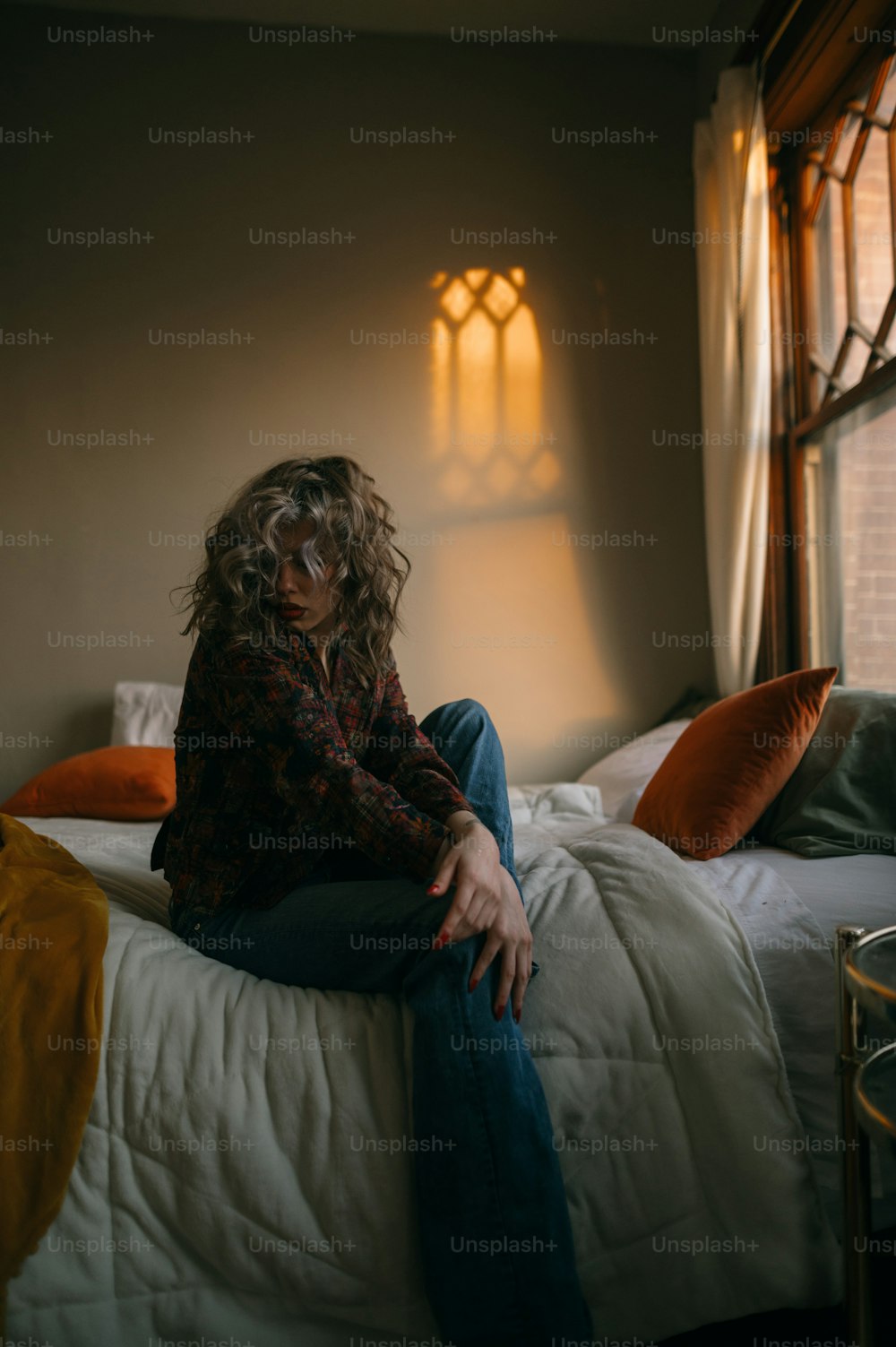 Una mujer sentada encima de una cama junto a una ventana