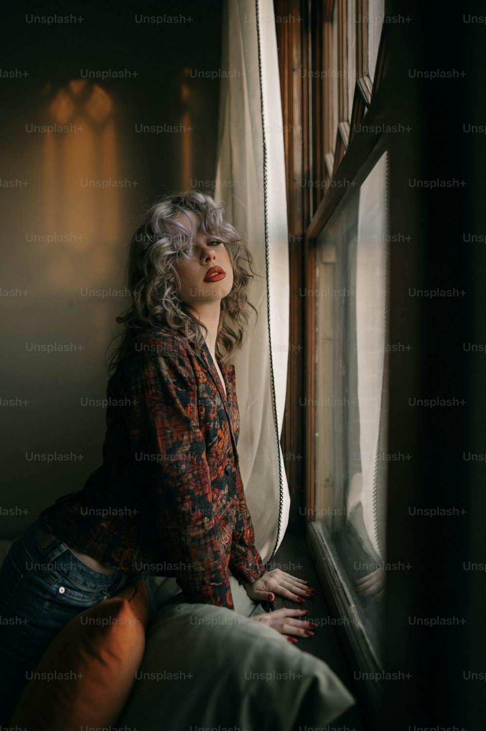 a woman sitting on a bed looking out of a window