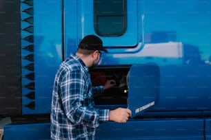 Un homme en chemise à carreaux ouvrant une porte bleue de camion