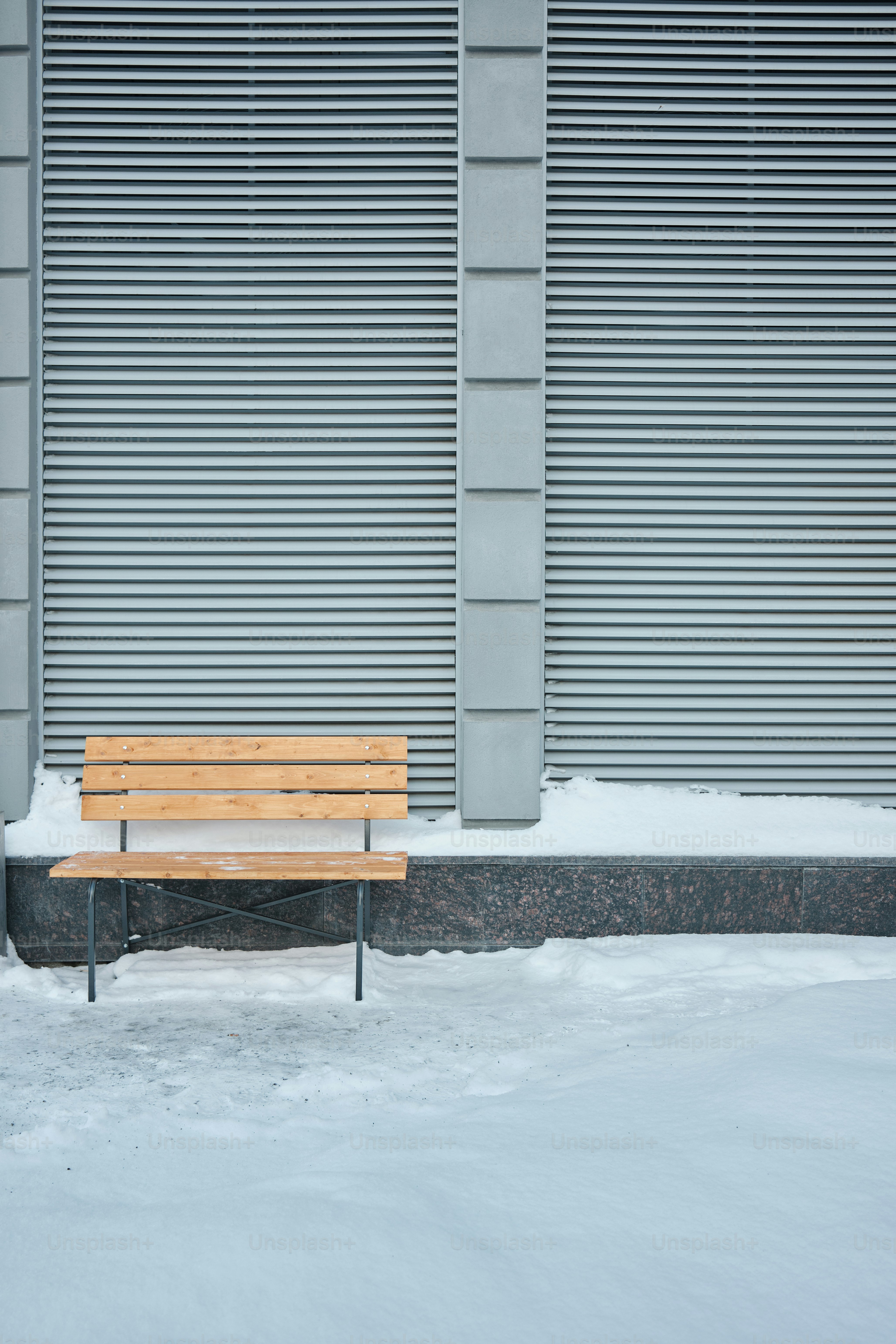 A bench in the snow against a geometric wall