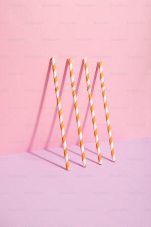 three orange and white striped straws on a pink background